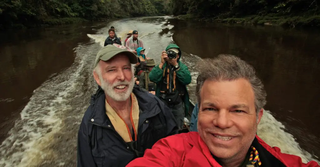 Group of hikers on a boat taking a selfie with the river and forest behind them in a lush setting.